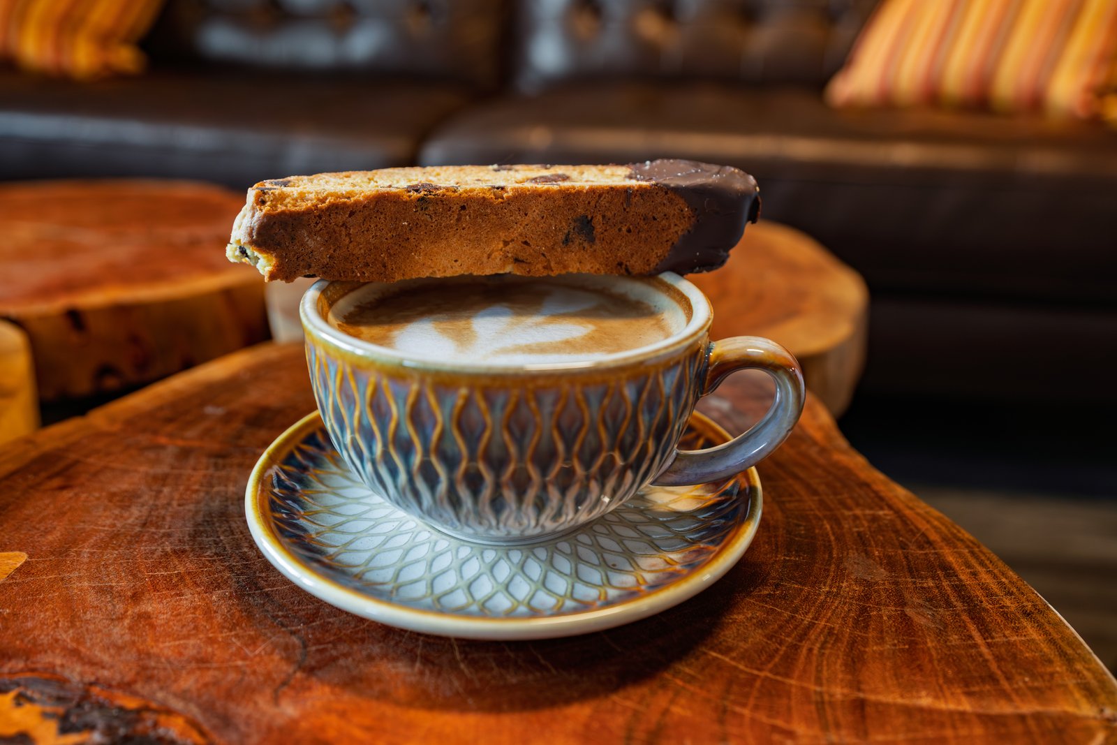 Chocolate-dipped biscotti resting on a patterned cappuccino cup