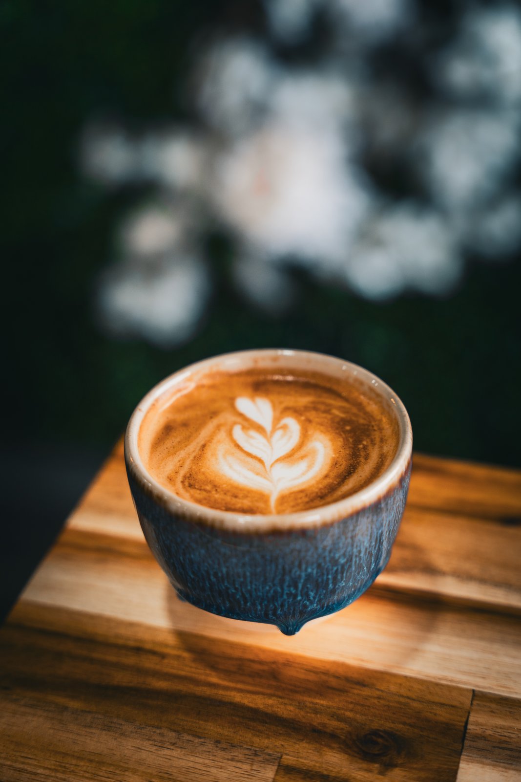 Latte art rosetta in a deep blue ceramic cup with a soft floral background