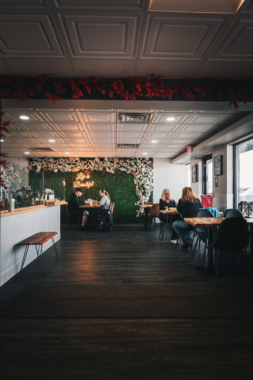 Perla dining room with the Life is Beautiful neon sign and floral wall, guests at tables