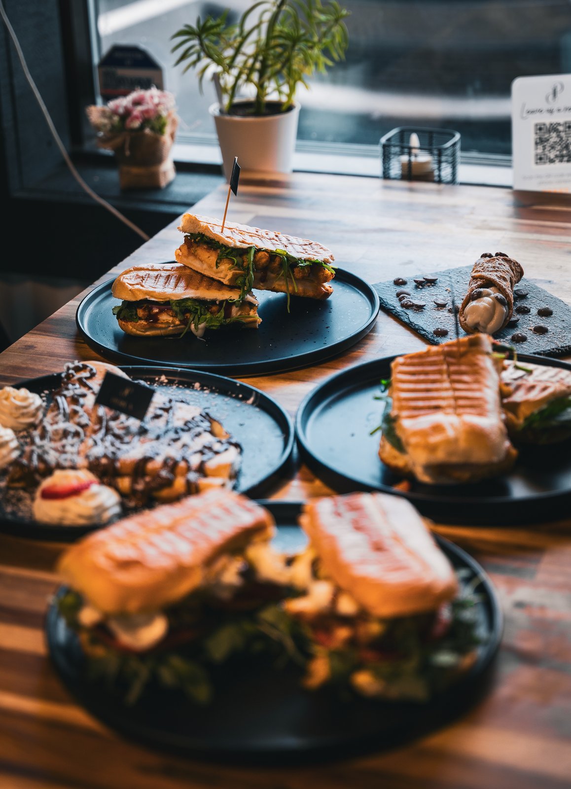 Spread of grilled paninis, cannoli, and waffles with chocolate drizzle on a wooden table