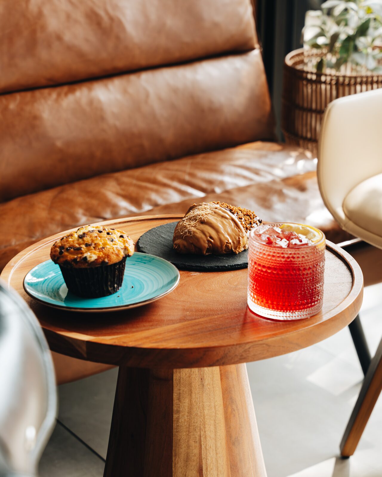 Muffin, dulce de leche pastry, and iced tea on a wooden side table by leather couch